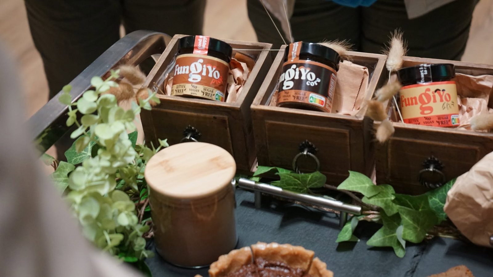 Borcanele produsului FungiYo, prezentate în lădițe de lemn cu decor vegetal